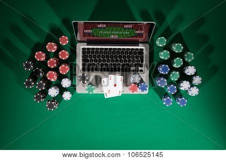 Poker chips and cards surrounding a laptop on a table.