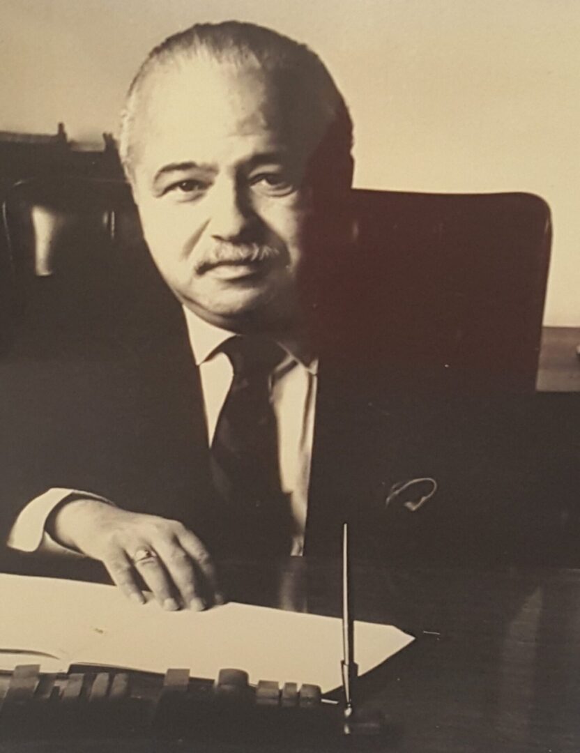 Black and white portrait of a man in a suit sitting at a desk.