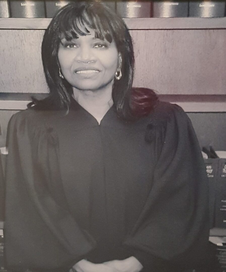 A woman judge in black robes posing indoors with a gentle smile.