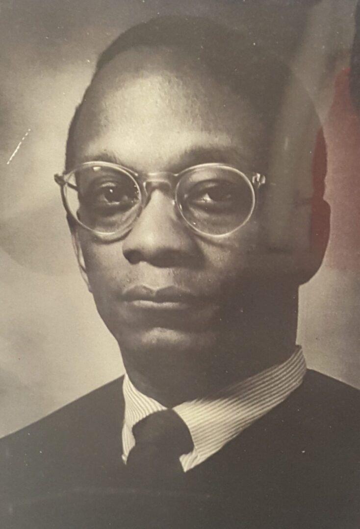 Black and white portrait of a man wearing glasses and a suit.