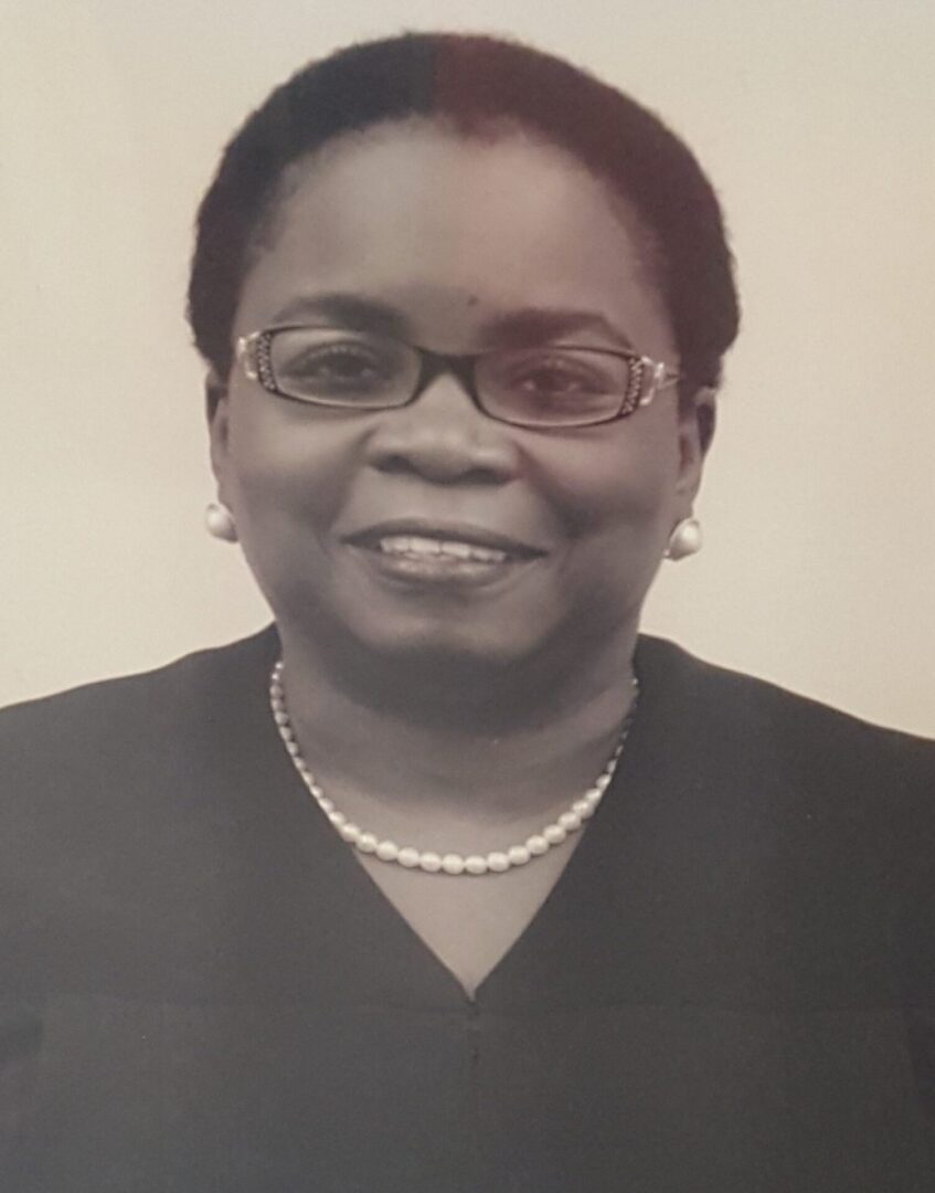 Black-and-white portrait of a smiling woman wearing glasses and a pearl necklace.