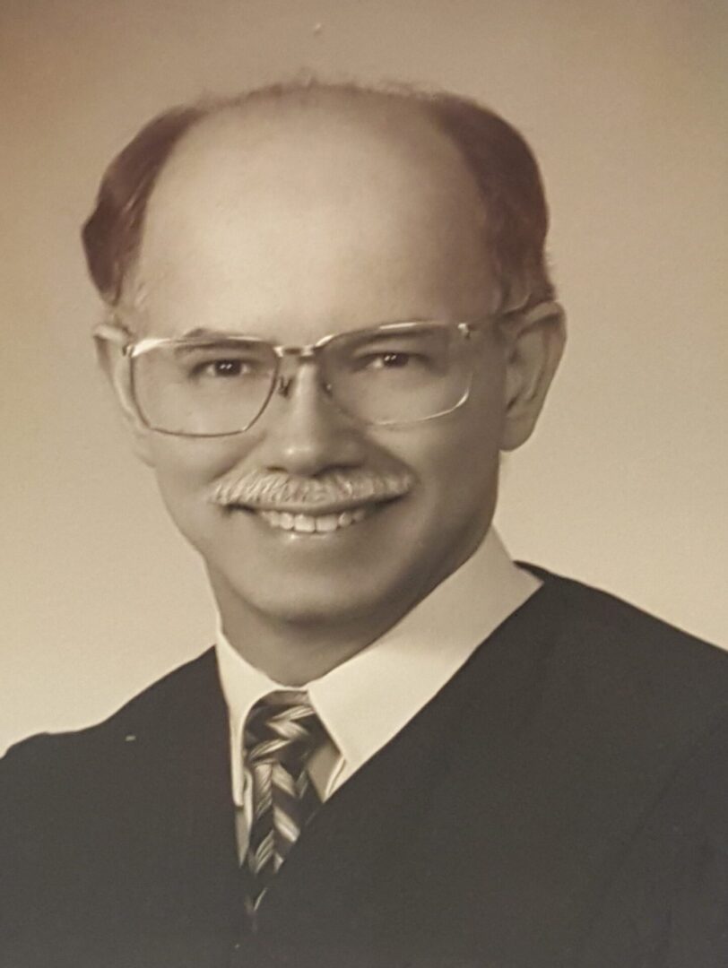 Portrait of a smiling man with glasses and a mustache in formal attire.