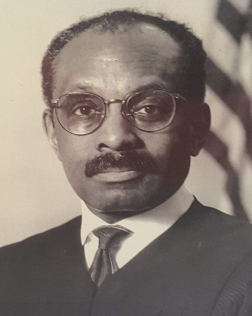 Black and white portrait of a man wearing glasses and a suit.