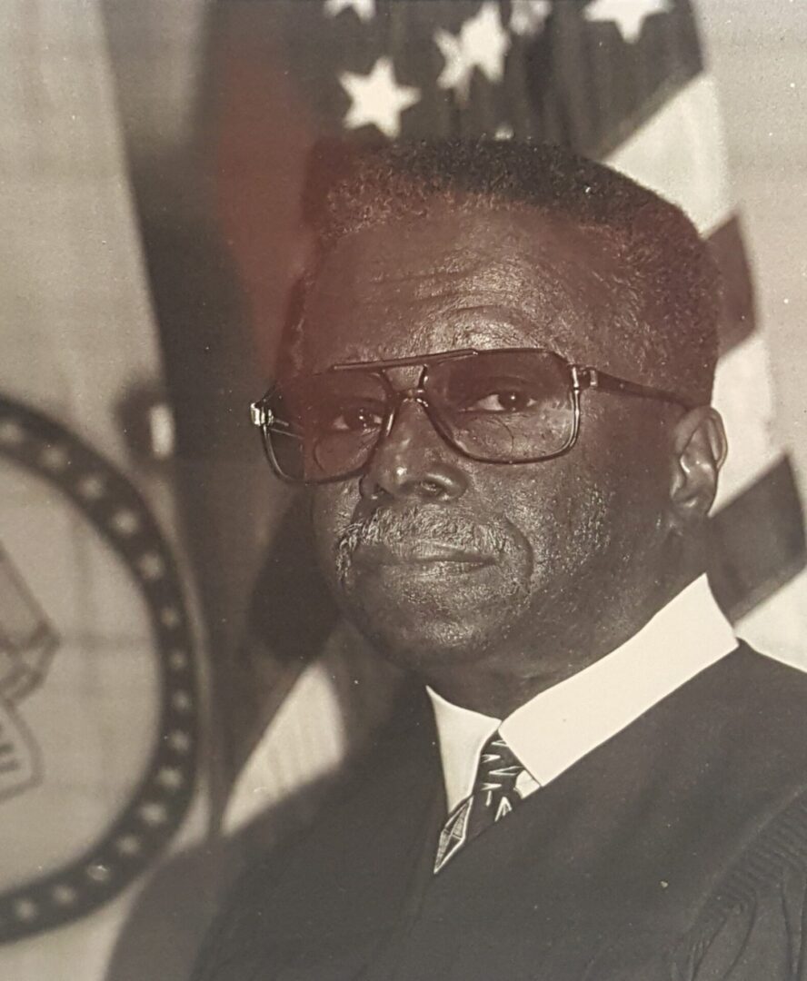 Black and white portrait of an elderly man wearing glasses and a suit.