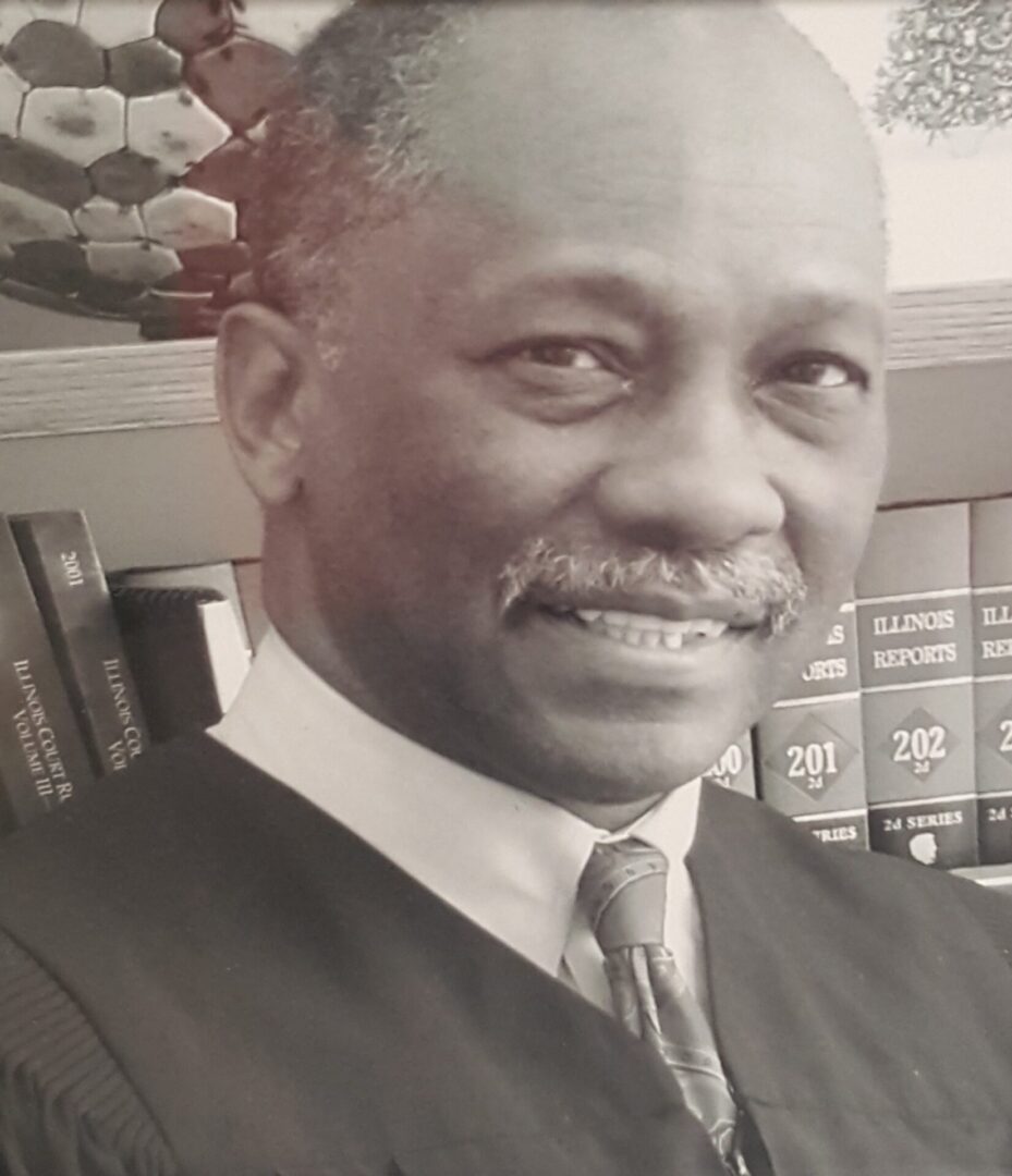Portrait of a smiling man in a suit with books in the background.
