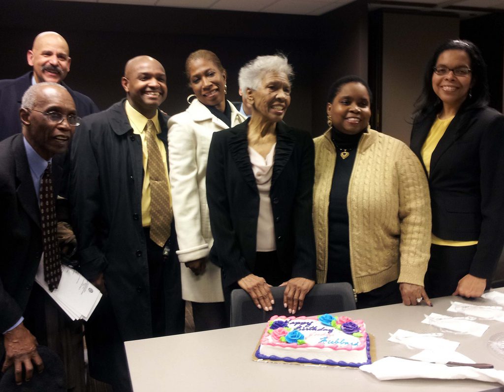 Group of people smiling around a decorated cake at a celebration.