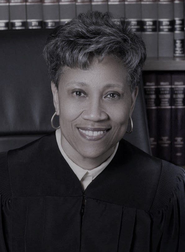 Smiling female judge in black robe, sitting in chambers.