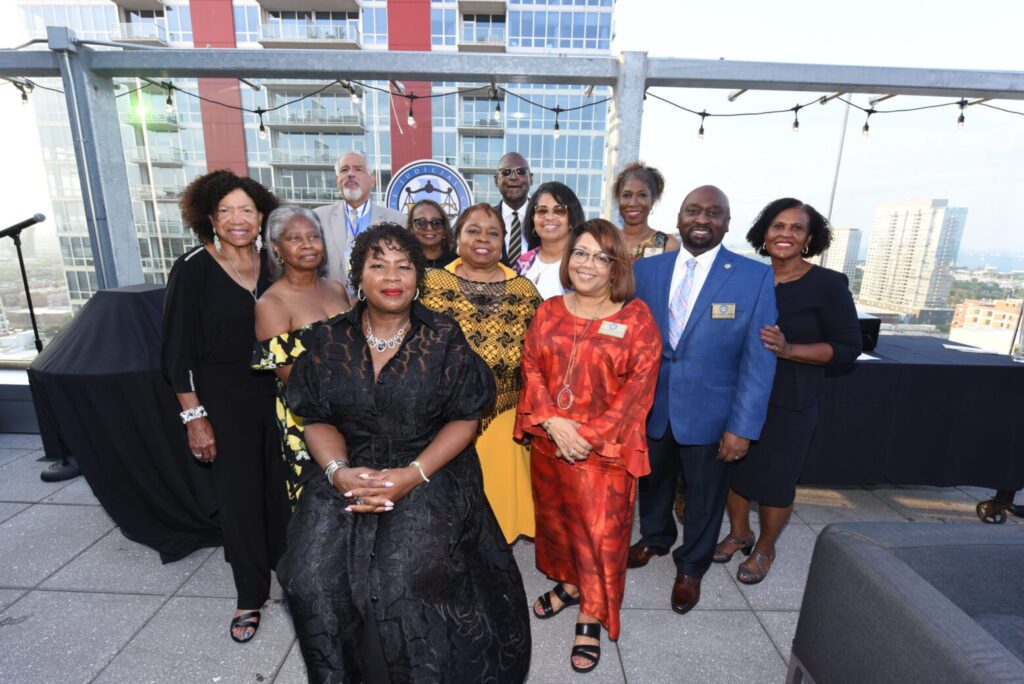 A diverse group posing together on a rooftop patio, dressed in formal and colorful attire.