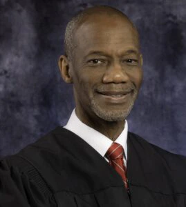 Portrait of a man in a judicial robe and red tie.