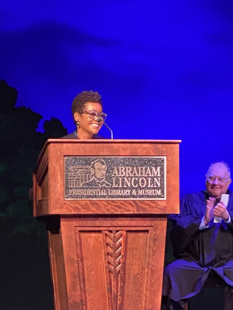 A woman speaking at a podium during an event at a library.
