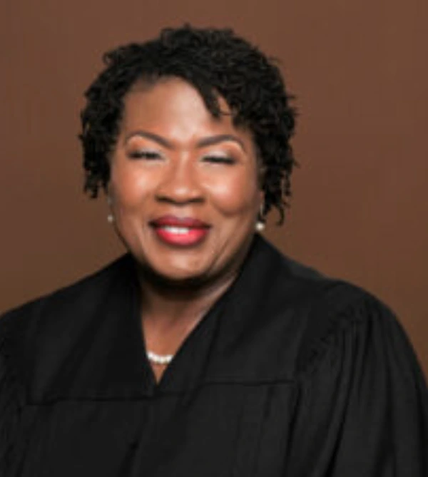 Smiling woman in judicial robe against brown background.
