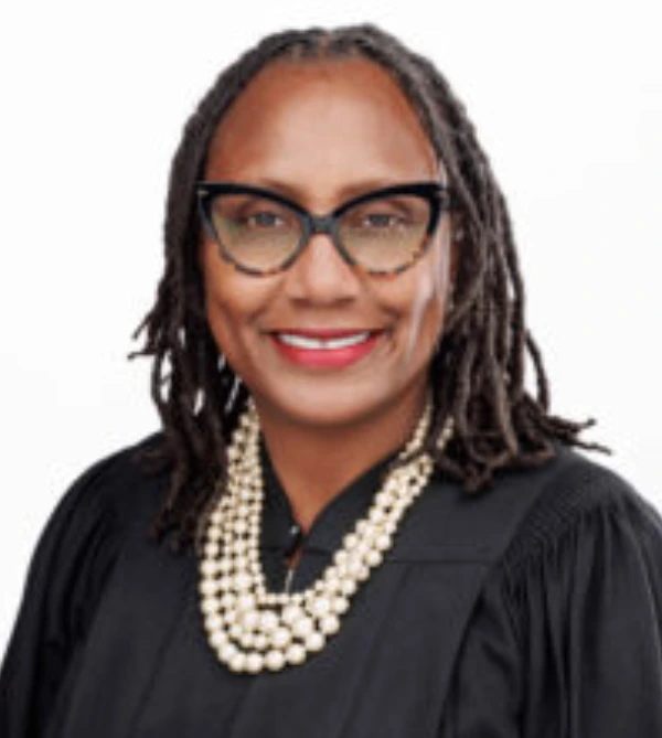 Professional woman with glasses and layered pearl necklace smiling.