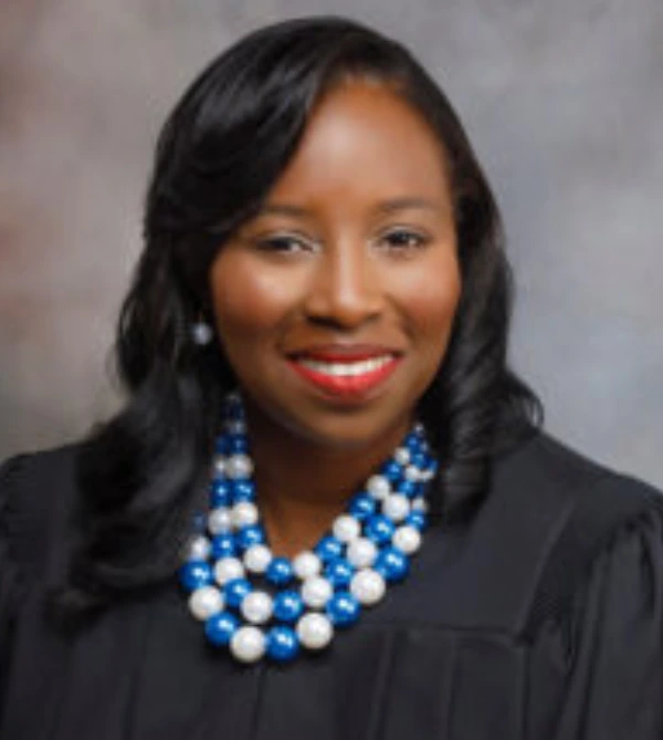 Professional woman smiling in formal attire with a pearl necklace.