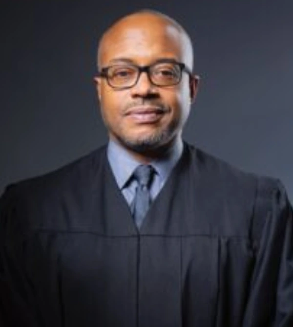 A confident man in judicial robes and glasses.