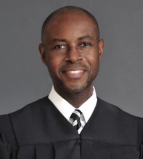 Portrait of a smiling judge in a black judicial robe.