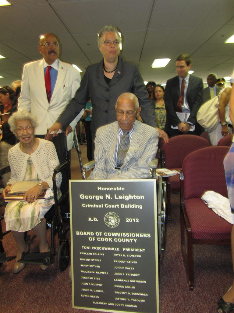 A group posing with a commemorative plaque in a formal indoor setting.