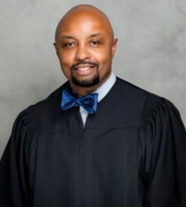 Man in black academic gown and blue bow tie smiling.