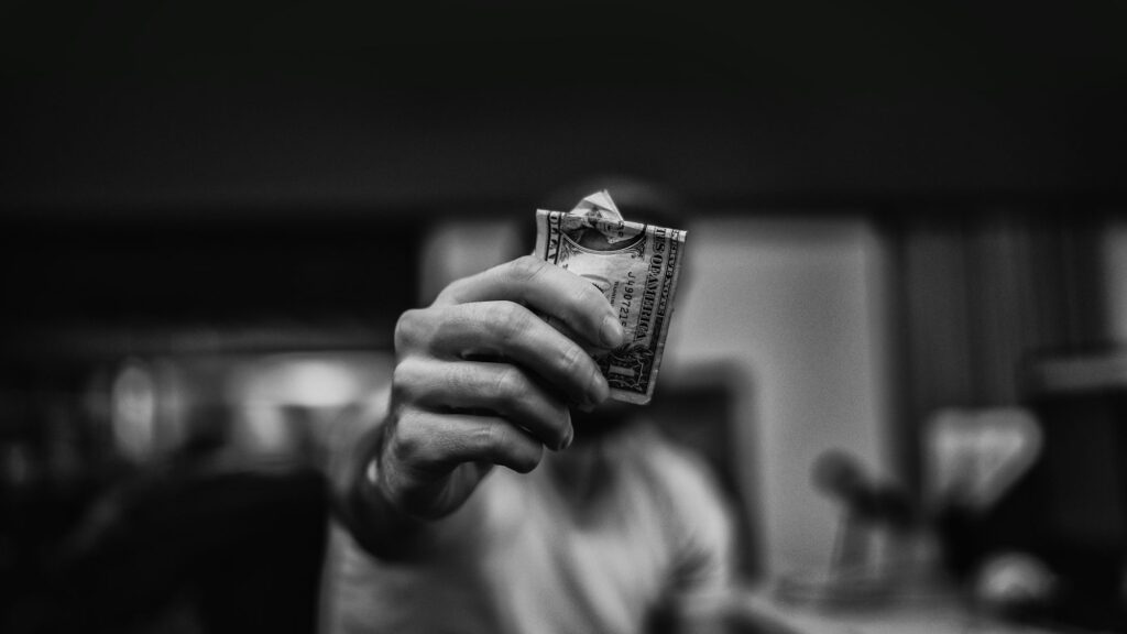 A person holding a folded dollar bill in focus, blurred background.