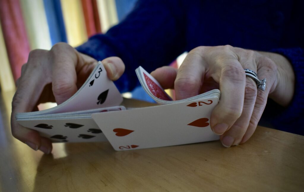 Hands shuffling a deck of playing cards on a wooden table.