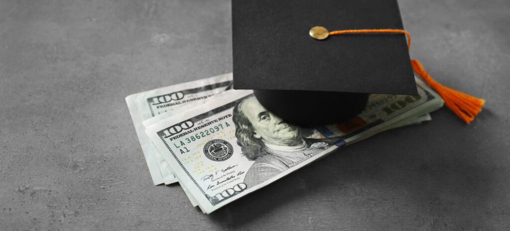 Graduation cap on hundred-dollar bills symbolizing financial success.