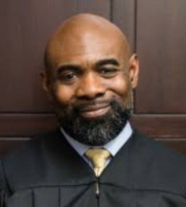 Smiling judge in black robe against wooden background.