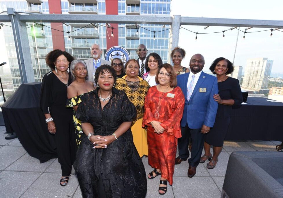 A diverse group posing together on a rooftop patio, dressed in formal and colorful attire.