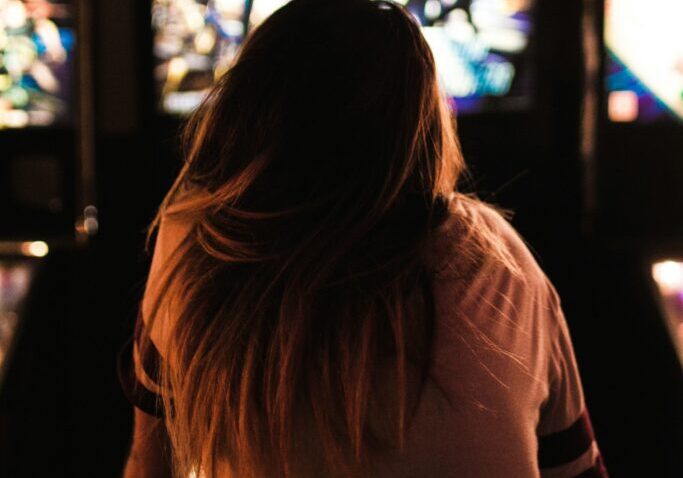 A person with long hair sitting indoors near stained glass windows.