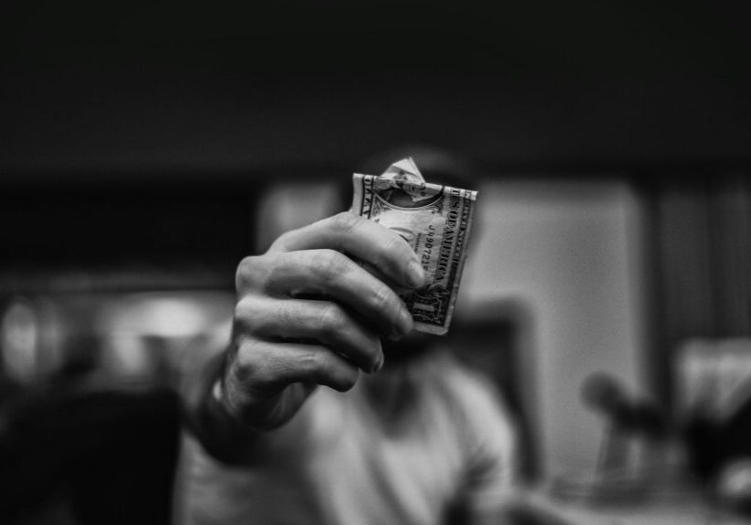 A person holding a folded dollar bill in focus, blurred background.