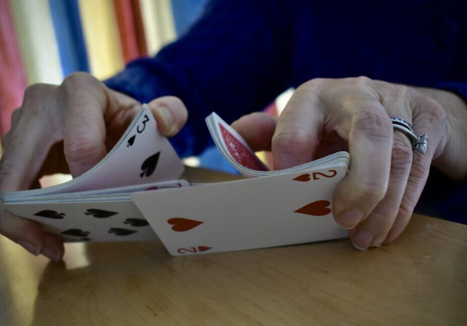 Hands shuffling a deck of playing cards on a wooden table.